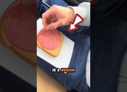 Enlace a Colando una rebanada de pan con una loncha de salami como obra de arte en un museo